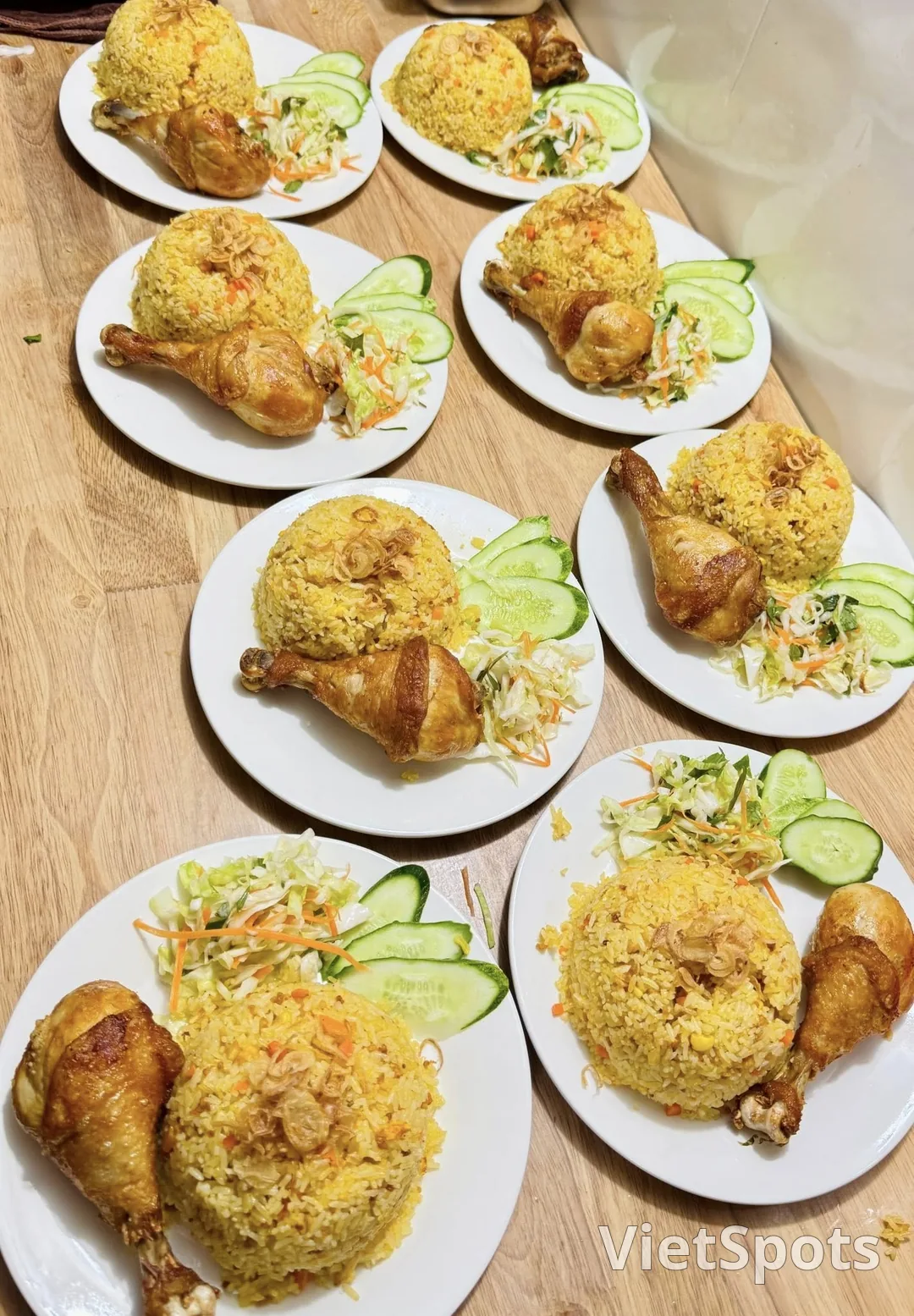 Nhiều đĩa cơm gà Việt Nam — cơm vàng nghệ, đùi gà, dưa leo, salad