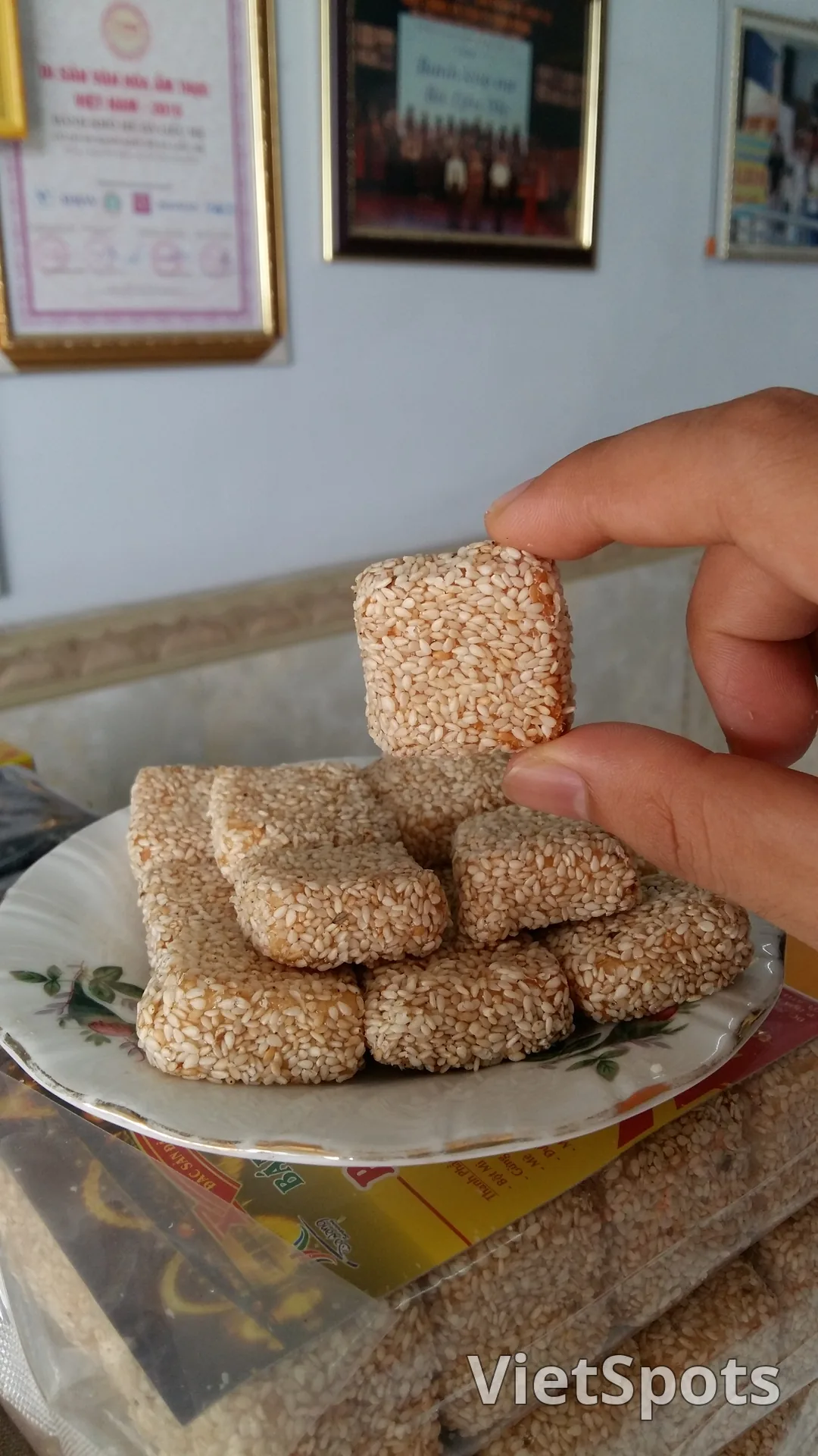 Nhiều miếng bánh khô mè vuông nhỏ phủ mè trắng rang, đựng trong đĩa hoa