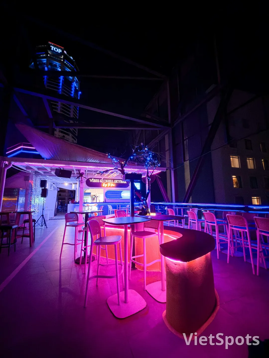 Rooftop skybar VIBES CHILL SKYBAR đêm với neon hồng-xanh + ghế bar cao + view tòa cao tầng TOP
