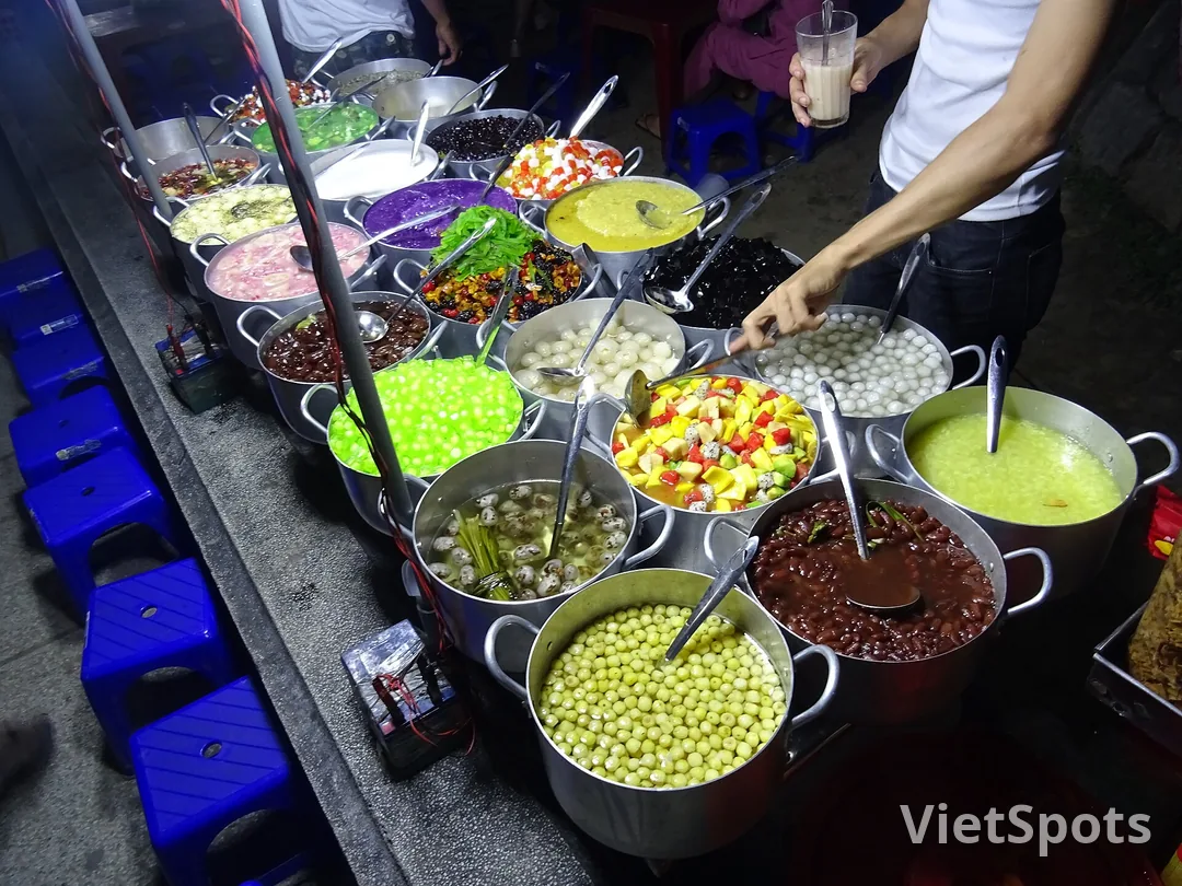 Xe chè với hơn hai chục nồi nhôm xếp kín, mỗi nồi một loại chè khác màu, người bán đang múc