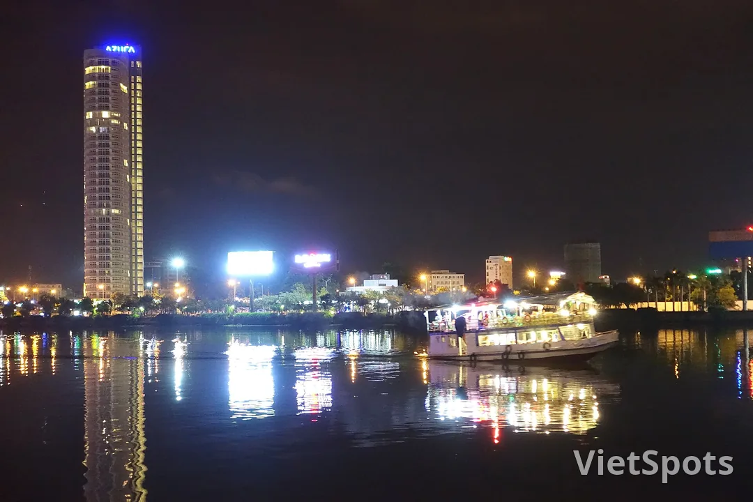 Một chiếc tàu du lịch đậu bên bờ sông Hàn ban đêm, đèn thành phố hắt thành vệt dài trên mặt nước