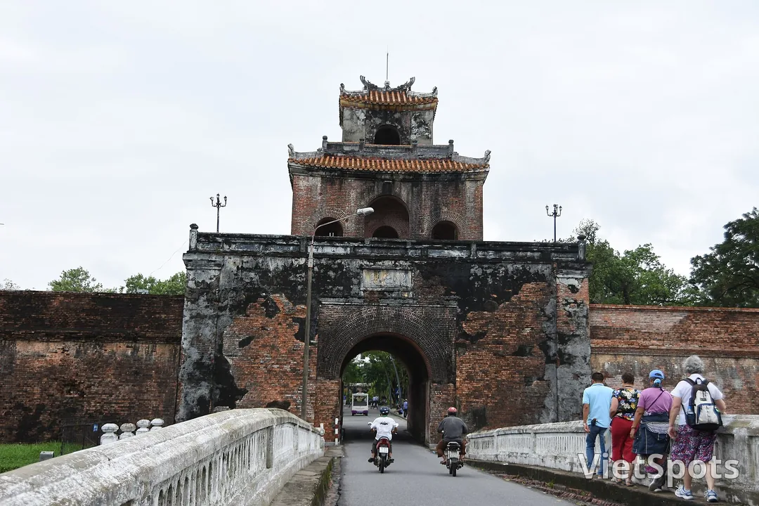 Cổng gạch cổ của Kinh thành Huế, tường rêu loang lổ, xe máy chạy qua vòm cổng