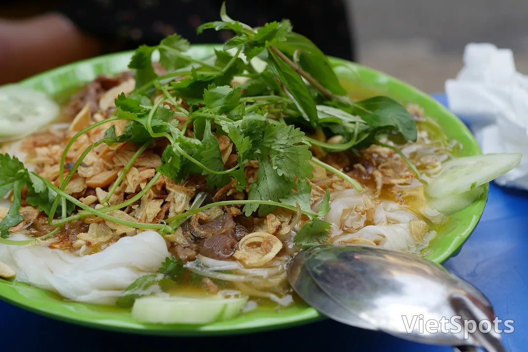 Đĩa bánh cuốn trắng mềm rắc hành phi vàng, phủ rau thơm và ngò, kèm mấy lát dưa leo