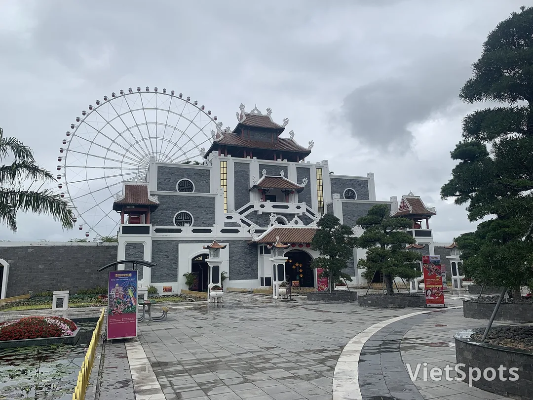Cổng công viên Asia Park Đà Nẵng với vòng quay Sun Wheel trắng phía sau, toà nhà mái ngói kiểu Á Đông, sân lát đá ướt mưa