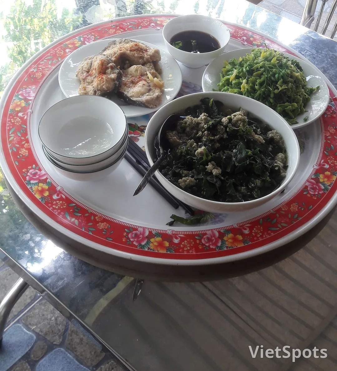 Mâm cơm gia đình Việt Nam trên khay nhựa viền đỏ: đĩa cá kho, tô canh rau, đĩa rau xào, chén nước chấm và mấy cái chén nhỏ xếp chồng