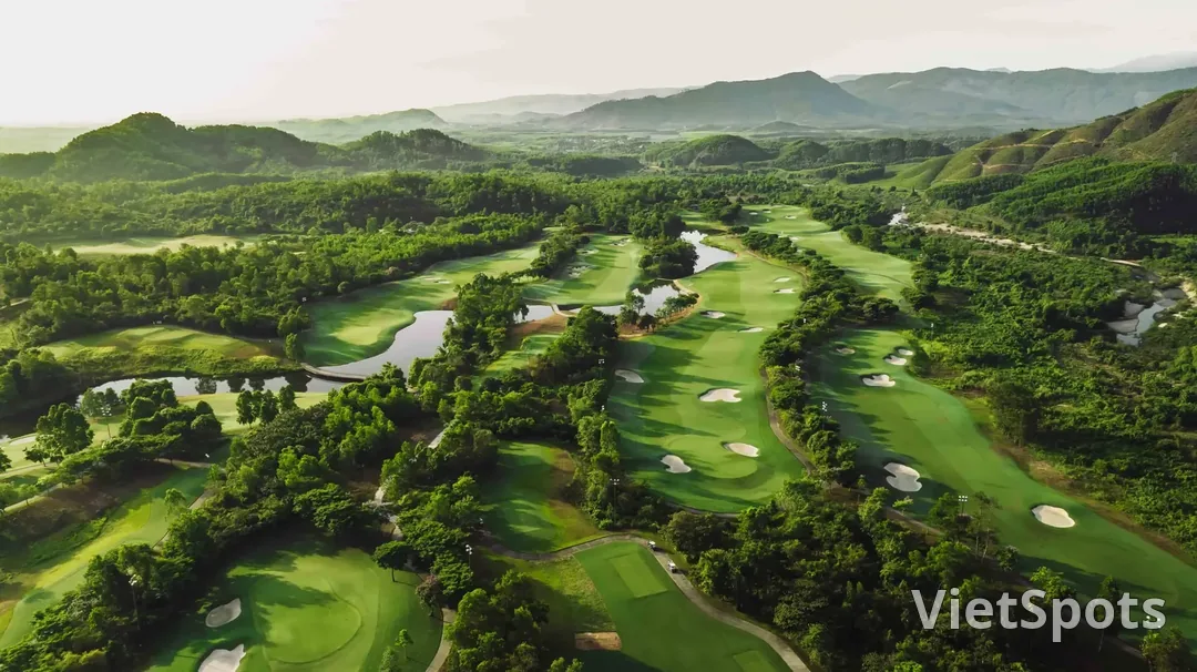 Toàn cảnh sân golf Bà Nà Hills nhìn từ trên cao, các fairway xanh luồn giữa đồi rừng, phía sau là dãy núi trùng điệp