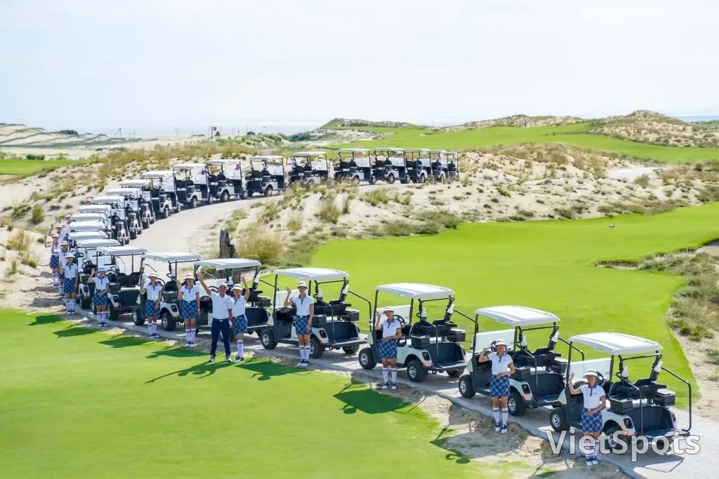 Đoàn xe điện xếp hàng dài trước giờ ra sân ở Hoiana Shores, các caddie mặc đồng phục đứng bên cạnh vẫy tay