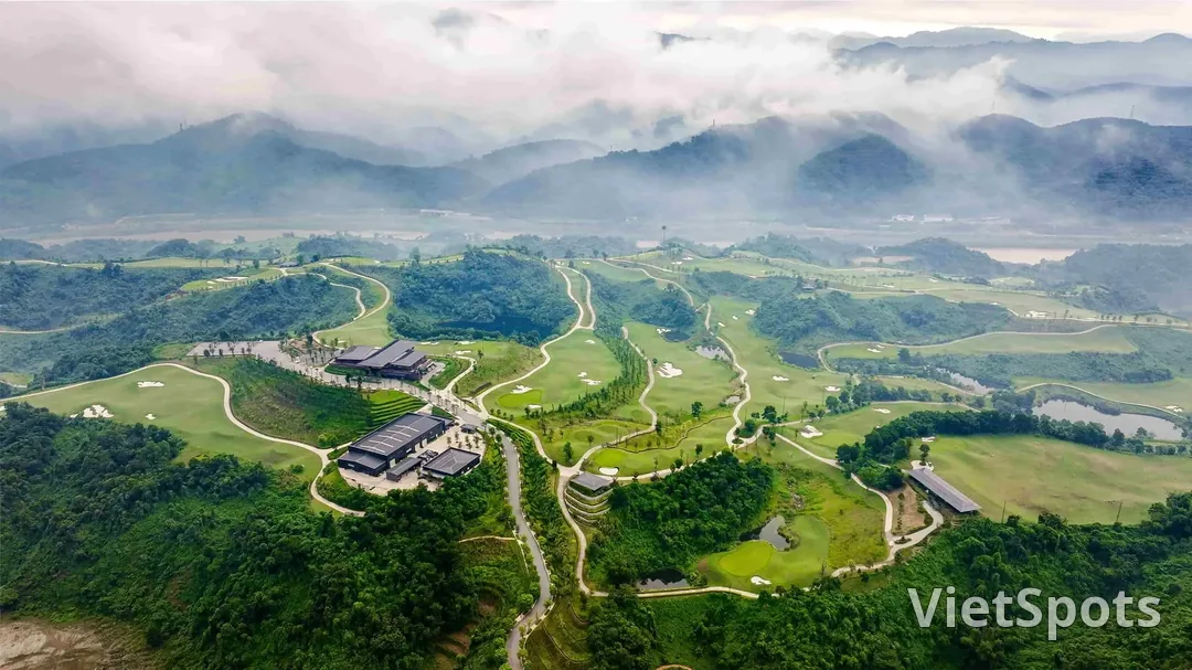 Sân Sapa Grand nhìn từ trên cao, các fairway uốn giữa đồi rừng với mây thấp phủ kín dãy núi phía sau