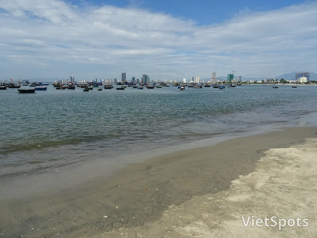 Mép nước bãi biển phía bắc Đà Nẵng lúc nước rút, ngoài khơi là hàng dài tàu cá và thuyền thúng neo trước dãy nhà cao tầng