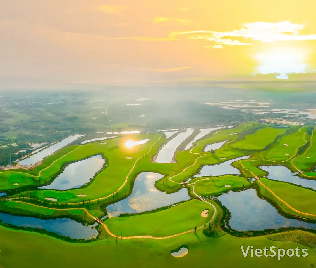 Toàn cảnh một sân golf nhìn từ trên cao lúc nắng vàng, các fairway xanh và hồ nước đan xen nhau trải tới tận chân trời