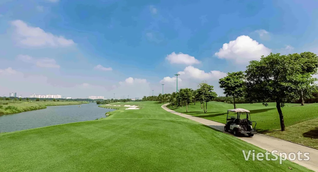 Fairway sân Long Biên chạy dọc một nhánh sông, xe điện đậu bên đường, phía xa là các khu nhà cao tầng của Hà Nội