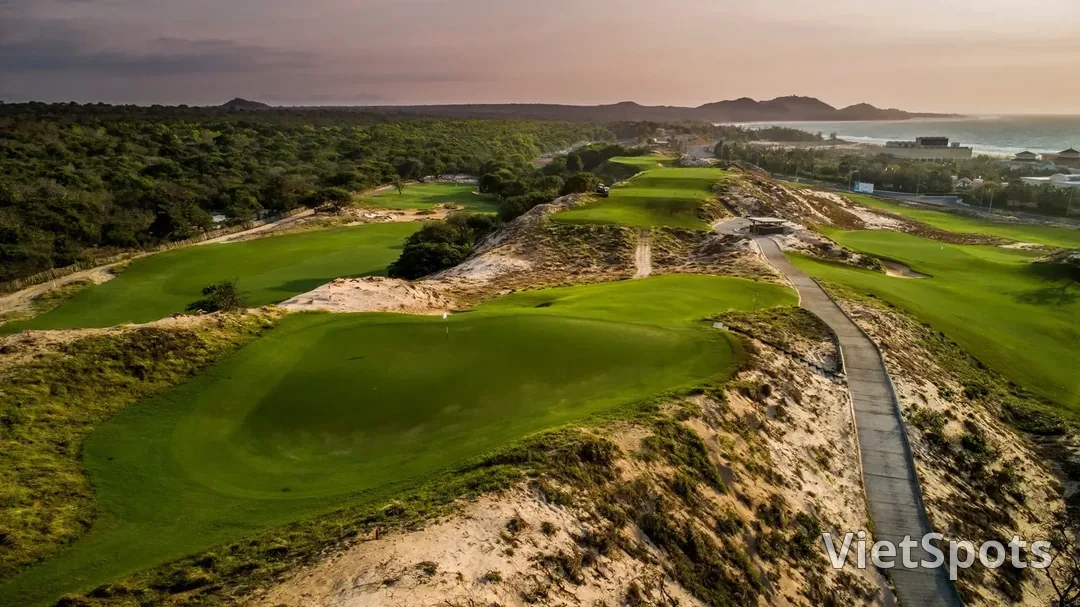 Sân The Bluffs Hồ Tràm lúc hoàng hôn, các green xanh nằm lọt giữa đồi cát lớn, biển trải dài phía sau
