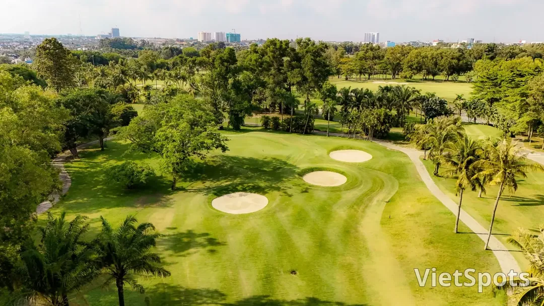 Fairway rợp bóng cây cổ thụ và hàng cau ở một sân golf ven Sài Gòn, phía chân trời là các toà nhà cao tầng