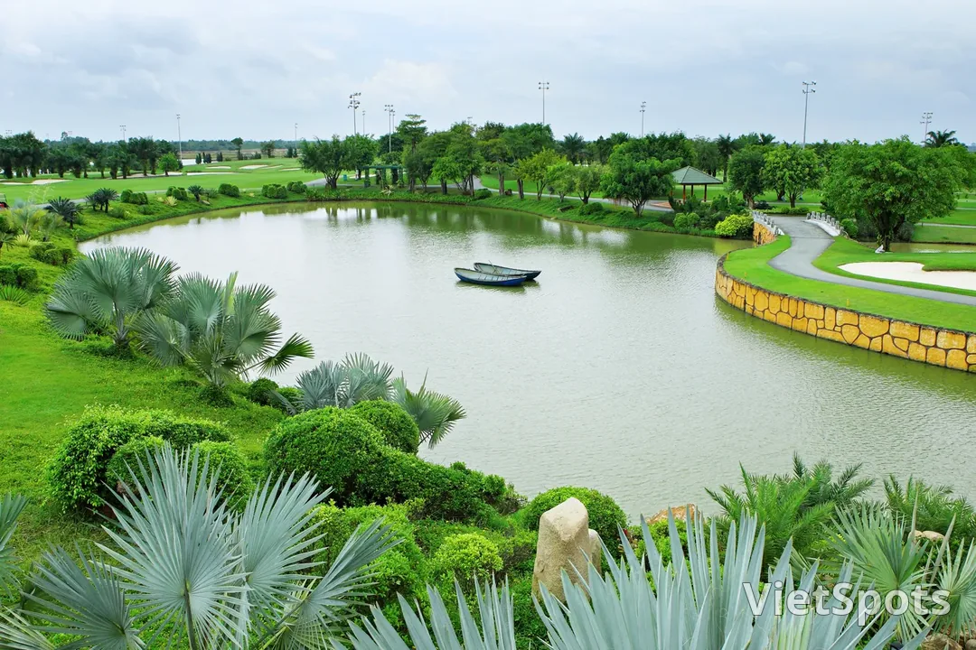 Hồ nước giữa sân golf với một chiếc thuyền nhỏ neo ở giữa, bờ hồ kè đá và trồng cọ xanh