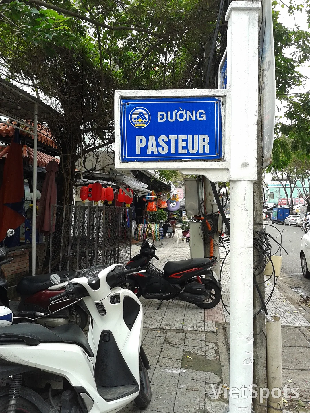 Biển tên đường Pasteur màu xanh có logo Đà Nẵng, phía dưới là xe máy đậu và quán treo đèn lồng đỏ