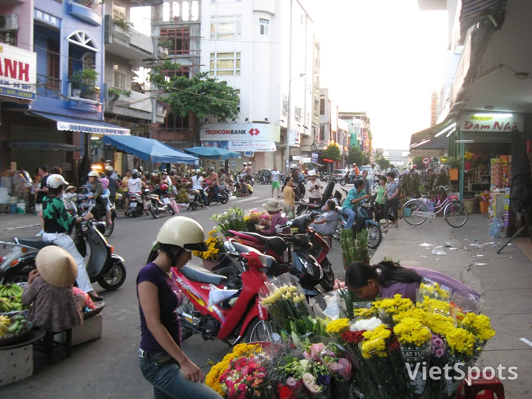 Hoa bán ngay trên vỉa hè trước chợ Hàn, Đà Nẵng: bó cúc vàng, hồng, ly xếp trên yên xe máy, người mua người bán chen nhau lúc chiều