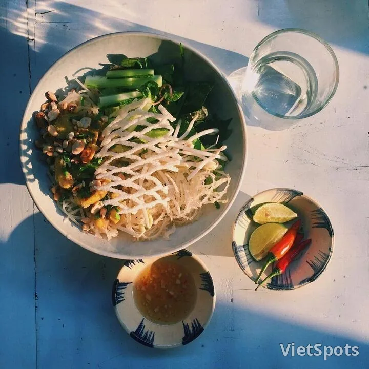 Phở sắn trộn khô với rau sống, giá, đậu phộng rang, chén nước mắm và dĩa ớt chanh bên cạnh