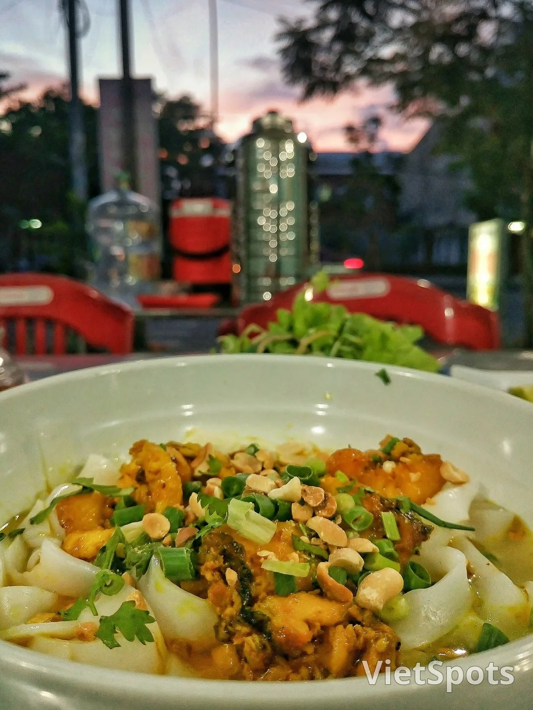 Tô mỳ Quảng cá lóc um nghệ ở Đà Nẵng, rắc đậu phộng và hành lá, phía sau là dĩa rau sống