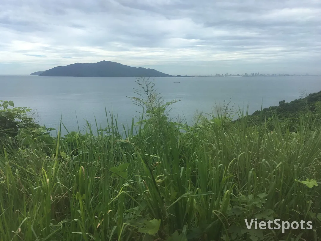 Bán đảo Sơn Trà nhìn từ bên kia vịnh Đà Nẵng: một khối núi xanh sẫm nổi trên mặt nước như hòn đảo, thành phố chỉ là một vệt nhà thấp ở phía xa bên phải