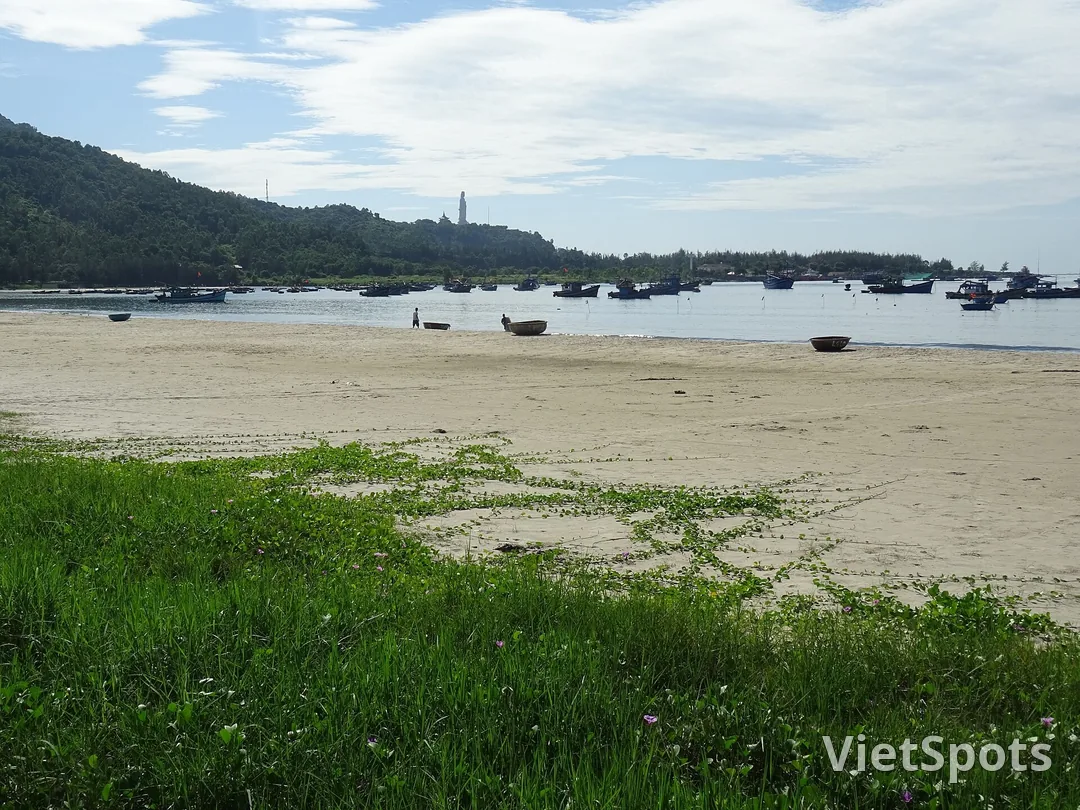 Bãi cát phía Mỹ Khê với thuyền thúng và thuyền đánh cá neo gần bờ, phía sau là núi Sơn Trà và tượng Phật Bà trắng trên sườn núi