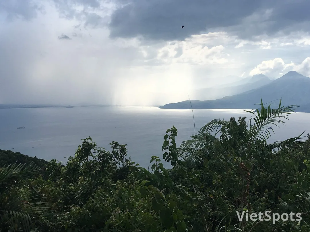 Từ trên núi Sơn Trà nhìn sang dãy Hải Vân bên kia vịnh, một cơn mưa rào đổ xuống mặt nước, nắng xuyên qua mây