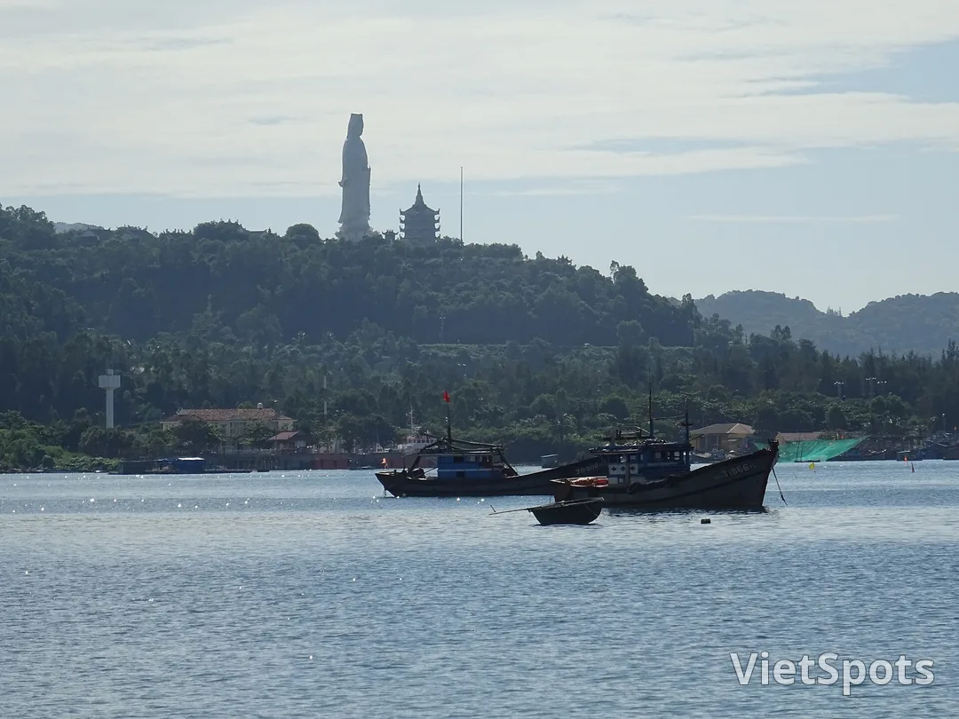 Tượng Phật Bà và tháp chùa Linh Ứng trên sườn Sơn Trà nhìn từ phía biển, dưới mặt nước là mấy chiếc thuyền đánh cá