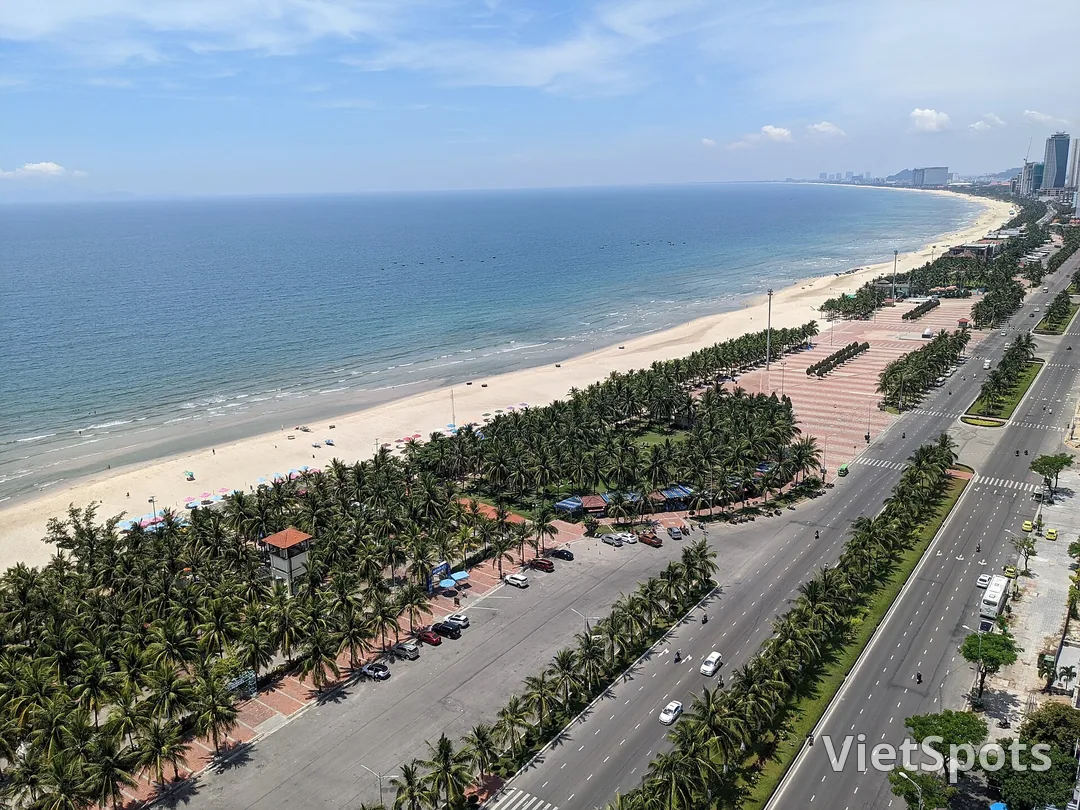 Nhìn từ trên cao xuống bờ biển Đà Nẵng: bãi cát dài cong về phía nam, hàng dừa và đường ven biển chạy song song