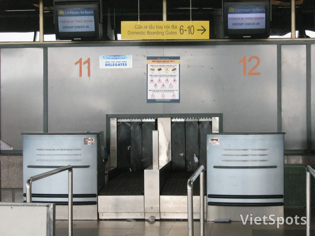 Quầy check-in sân bay Hà Nội với nhân viên hãng và bảng hiển thị thông tin chuyến bay quốc tế