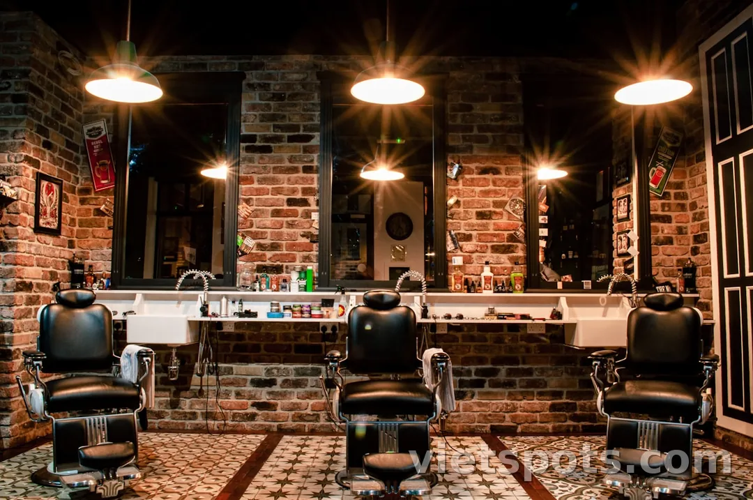 Barbershop interior — 3 ghế barber cổ điển, tường brick đỏ, đèn treo vàng