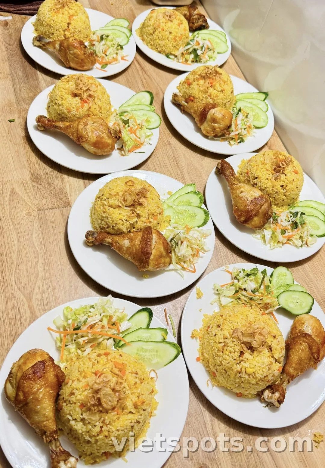 Nhiều đĩa cơm gà Việt Nam — cơm vàng nghệ, đùi gà, dưa leo, salad