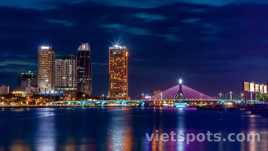 Sông Hàn Đà Nẵng ban đêm — Hilton + Novotel tower + Cầu Sông Hàn lên đèn tím phản chiếu trên mặt nước