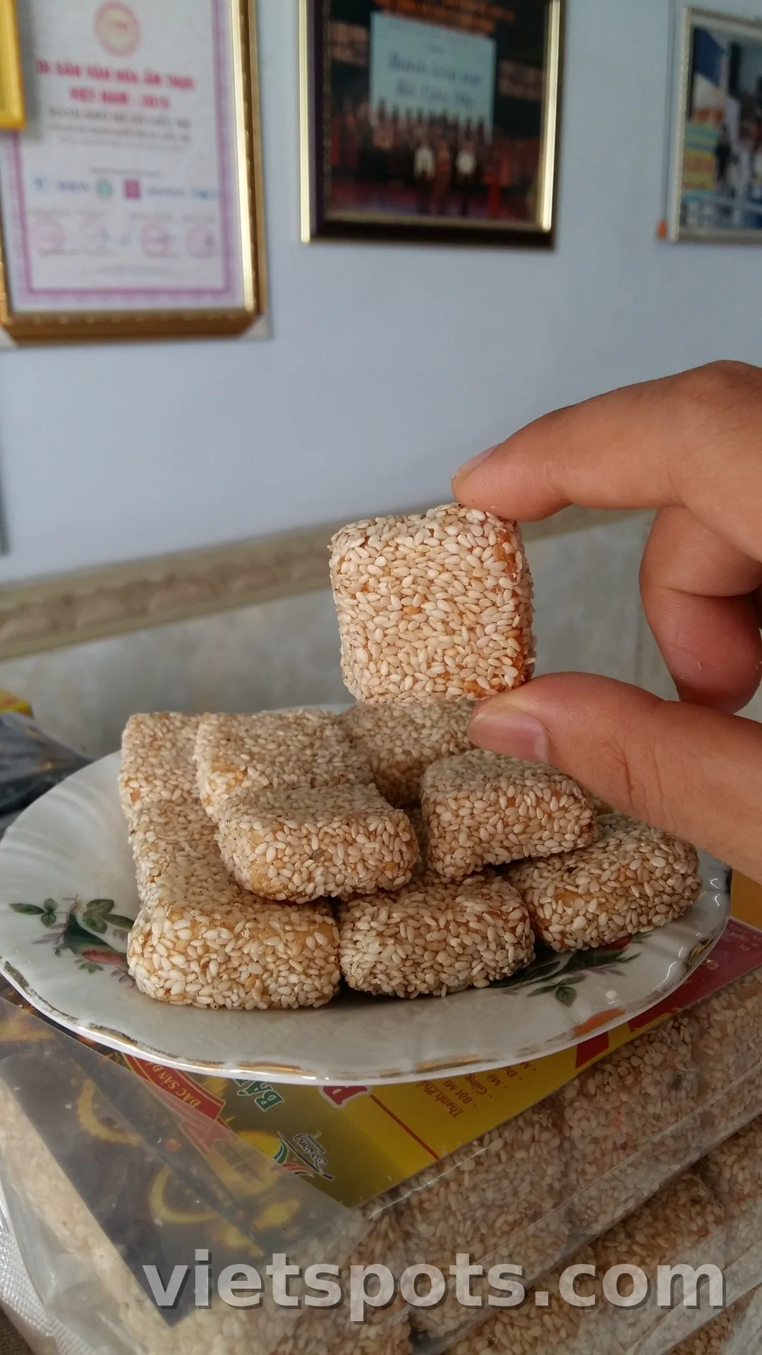 Nhiều miếng bánh khô mè vuông nhỏ phủ mè trắng rang, đựng trong đĩa hoa