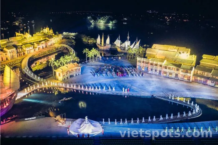 Aerial Ký Ức Hội An show 25.000m² — nhà cổ Hội An 2 bên, thuyền buồm, hàng cột trắng phun nước ánh sáng trên hồ, diễn viên áo dài đang biểu diễn giữa sân khấu