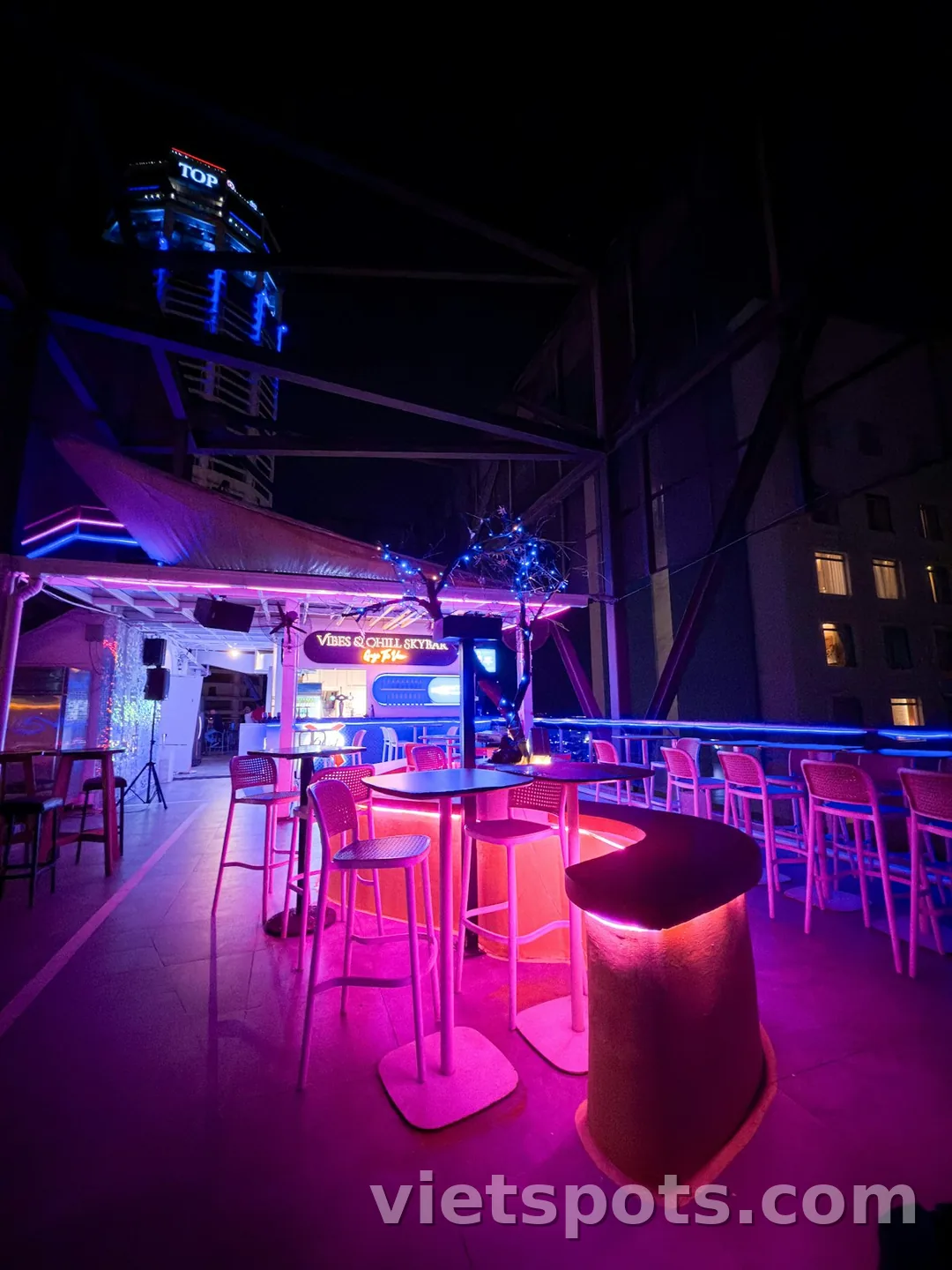 Rooftop skybar VIBES CHILL SKYBAR đêm với neon hồng-xanh + ghế bar cao + view tòa cao tầng TOP