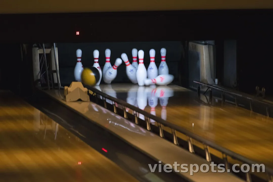 Bowling alley với bóng vàng vừa đánh trúng pin trắng đỏ, motion blur