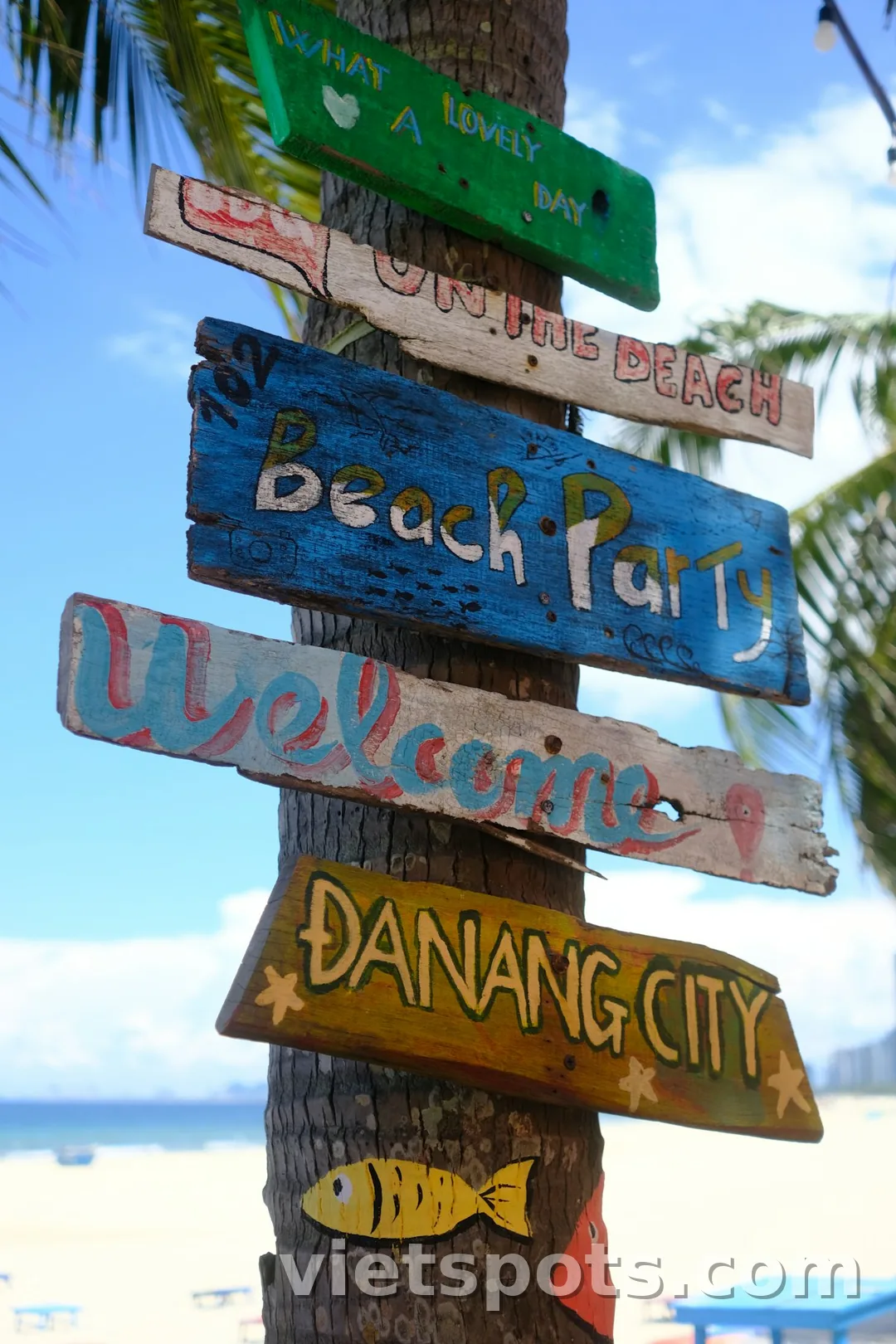 Cột gỗ ven biển Đà Nẵng có nhiều biển gỗ đủ màu Welcome, Beach Party, ĐANANG CITY — palm tree bên cạnh