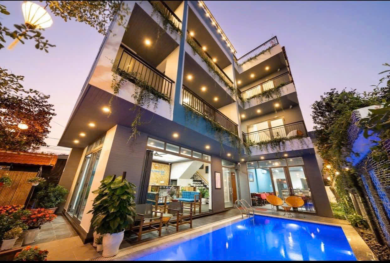 Villa bốn tầng lên đèn lúc chạng vạng, hồ bơi xanh ngay trước sân, ban công rủ cây xanh