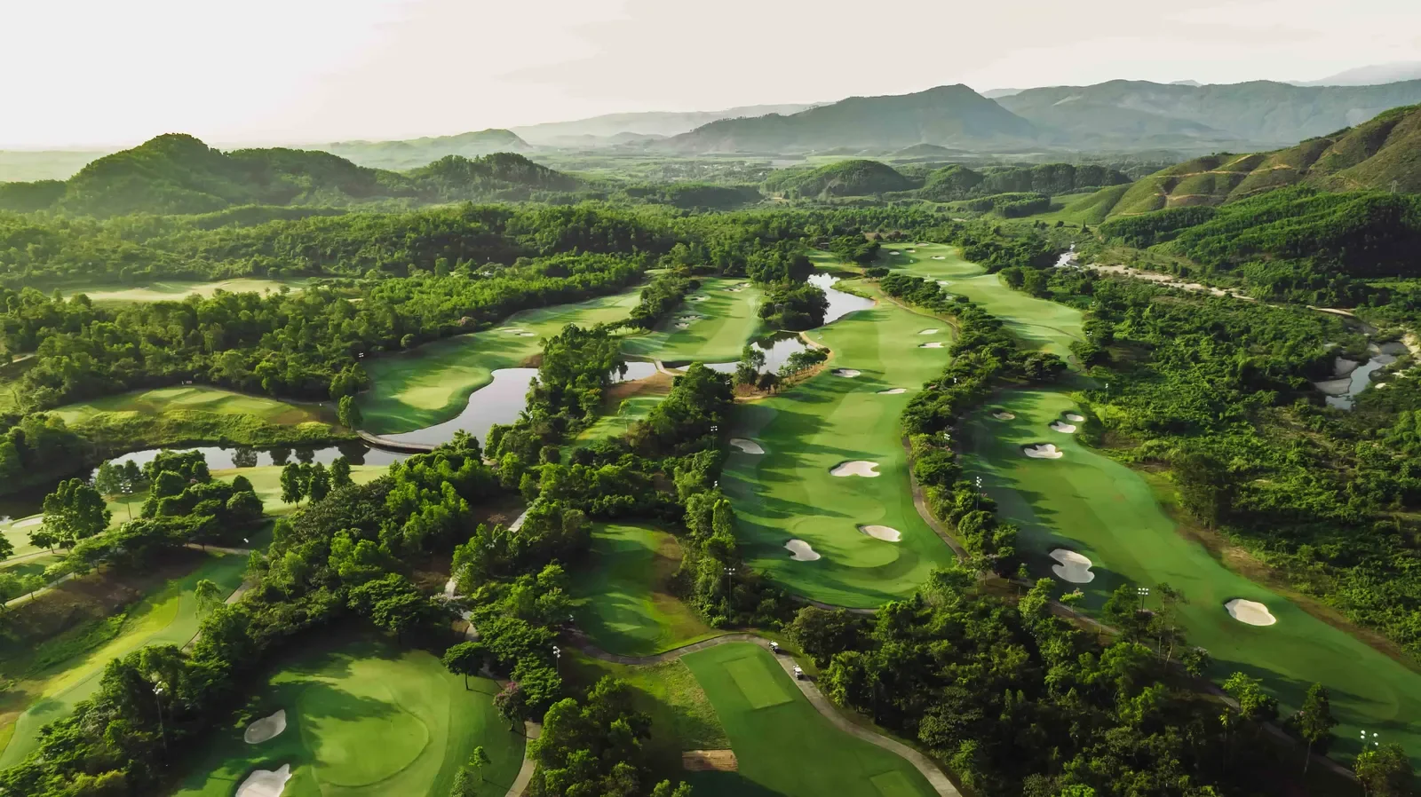Toàn cảnh sân golf Bà Nà Hills nhìn từ trên cao, các fairway xanh luồn giữa đồi rừng, phía sau là dãy núi trùng điệp