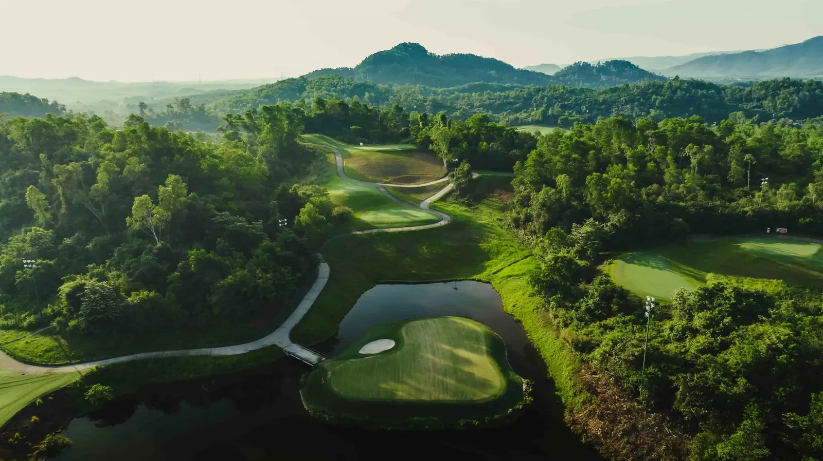 Green đảo của sân Bà Nà Hills nằm giữa hồ nước, bao quanh là rừng cây và các cột đèn chiếu sáng ban đêm