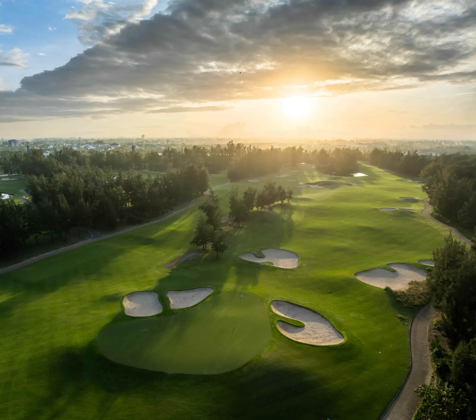 Sân Montgomerie Links nhìn từ trên cao lúc bình minh, nắng sớm xuyên qua rặng phi lao đổ bóng dài trên fairway
