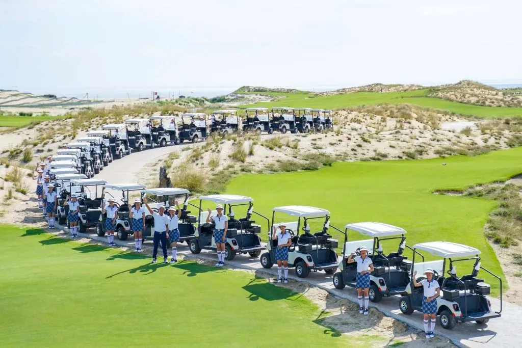Đoàn xe điện xếp hàng dài trước giờ ra sân ở Hoiana Shores, các caddie mặc đồng phục đứng bên cạnh vẫy tay